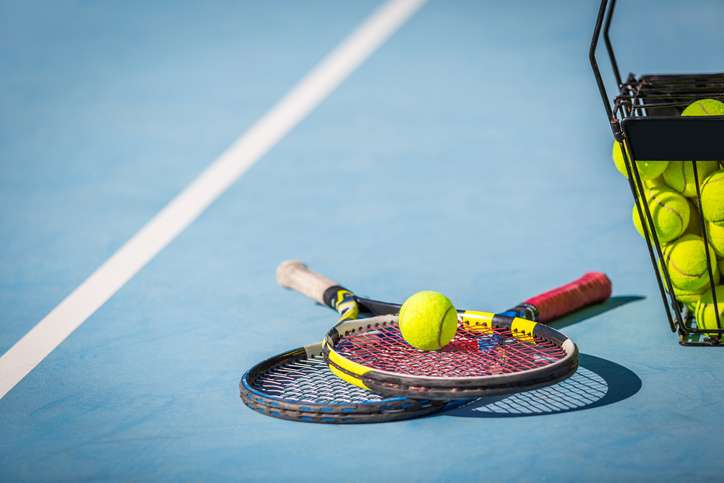 Two tennis rackets with a tennis ball sitting on top on a court